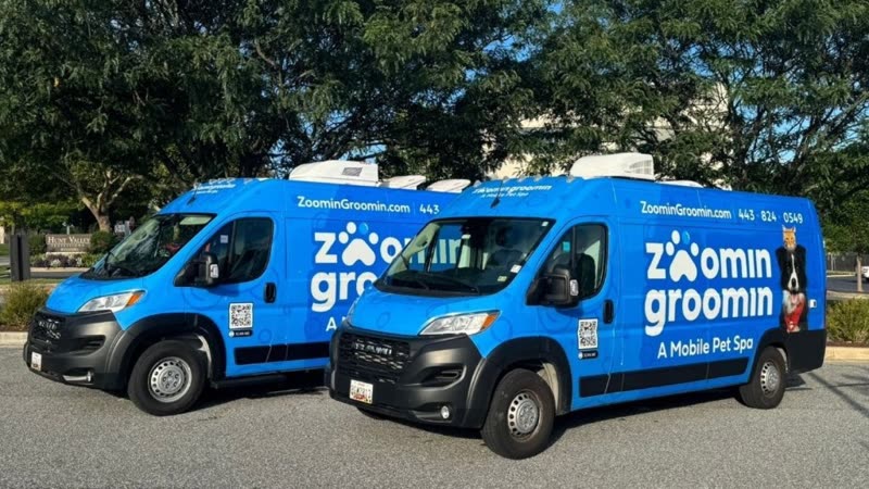 Two blue mobile grooming vans parked side by side under trees